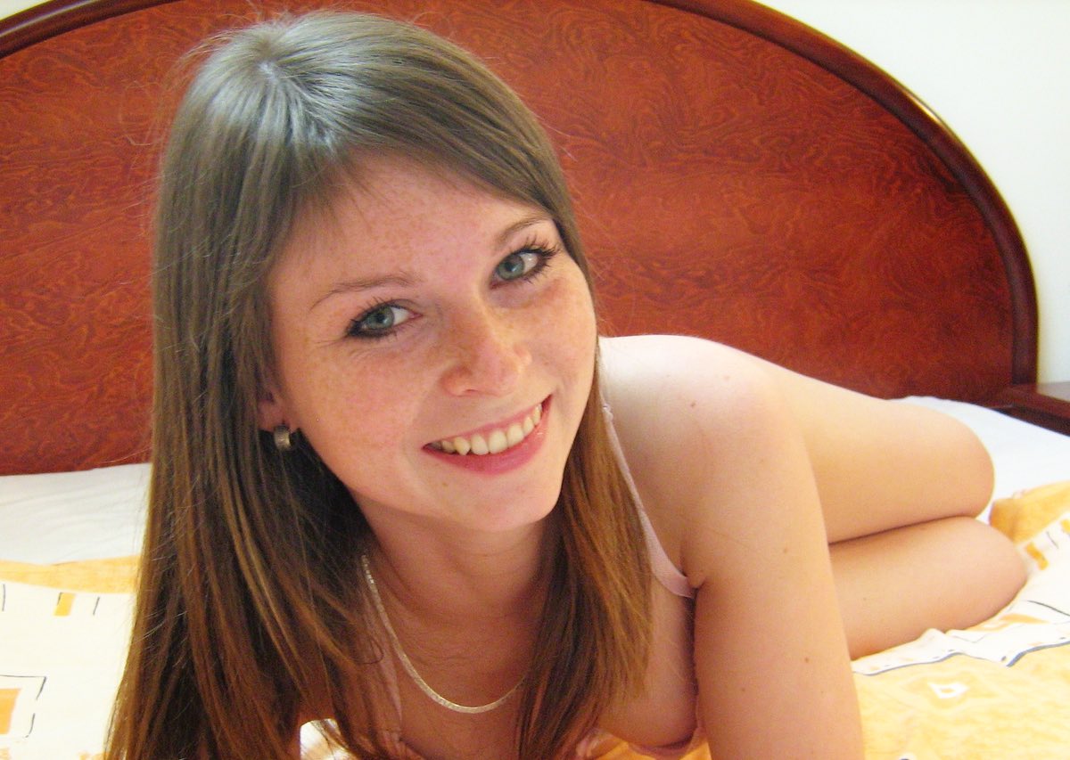 Jeune fille nue sur son lit, un beau sourire, des yeux verts et un visage plein de tâche de rousseur